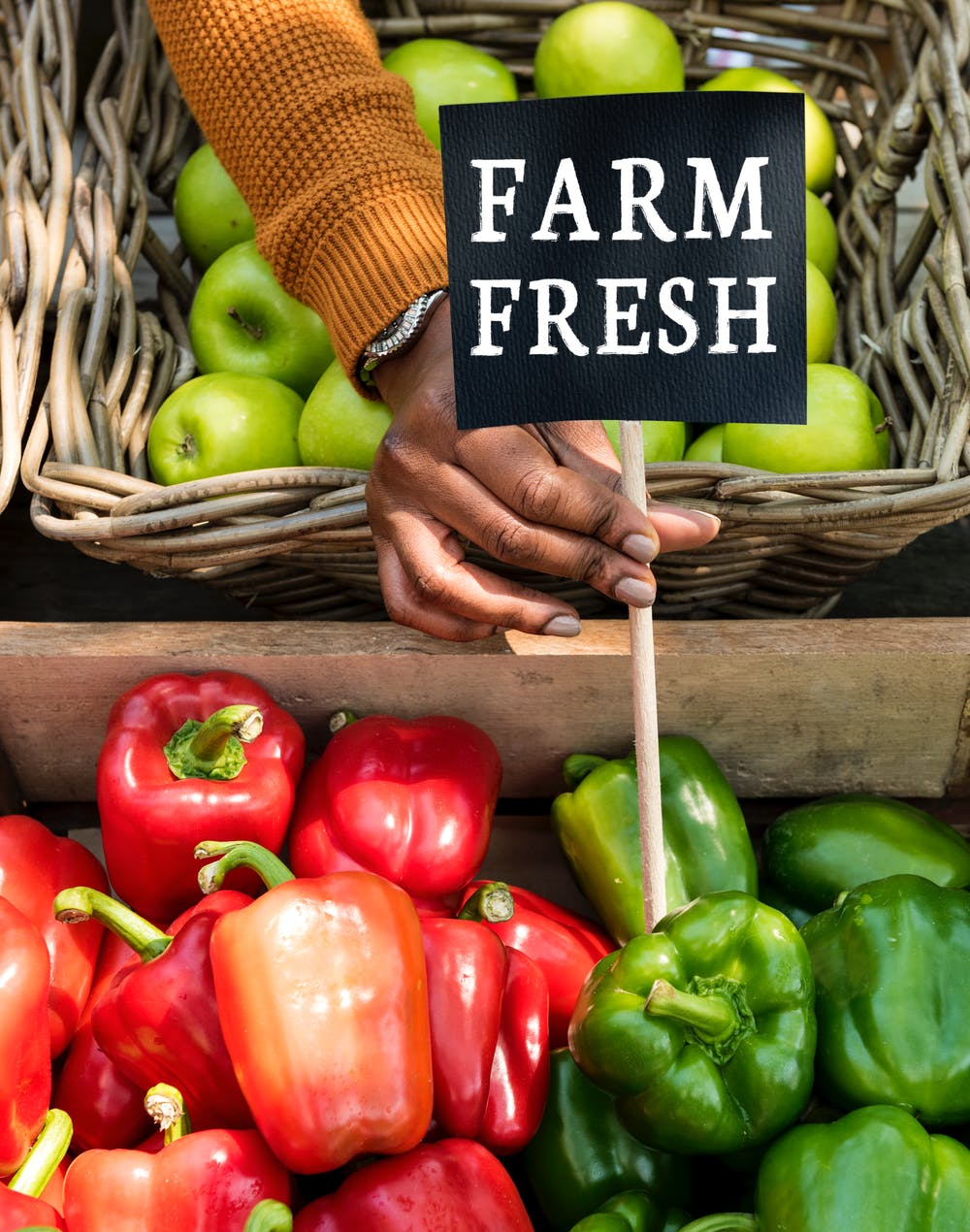 A shopper holding a hand-lettered &lsquo;Farm Fresh&rsquo; sign over crates of peppers and apples